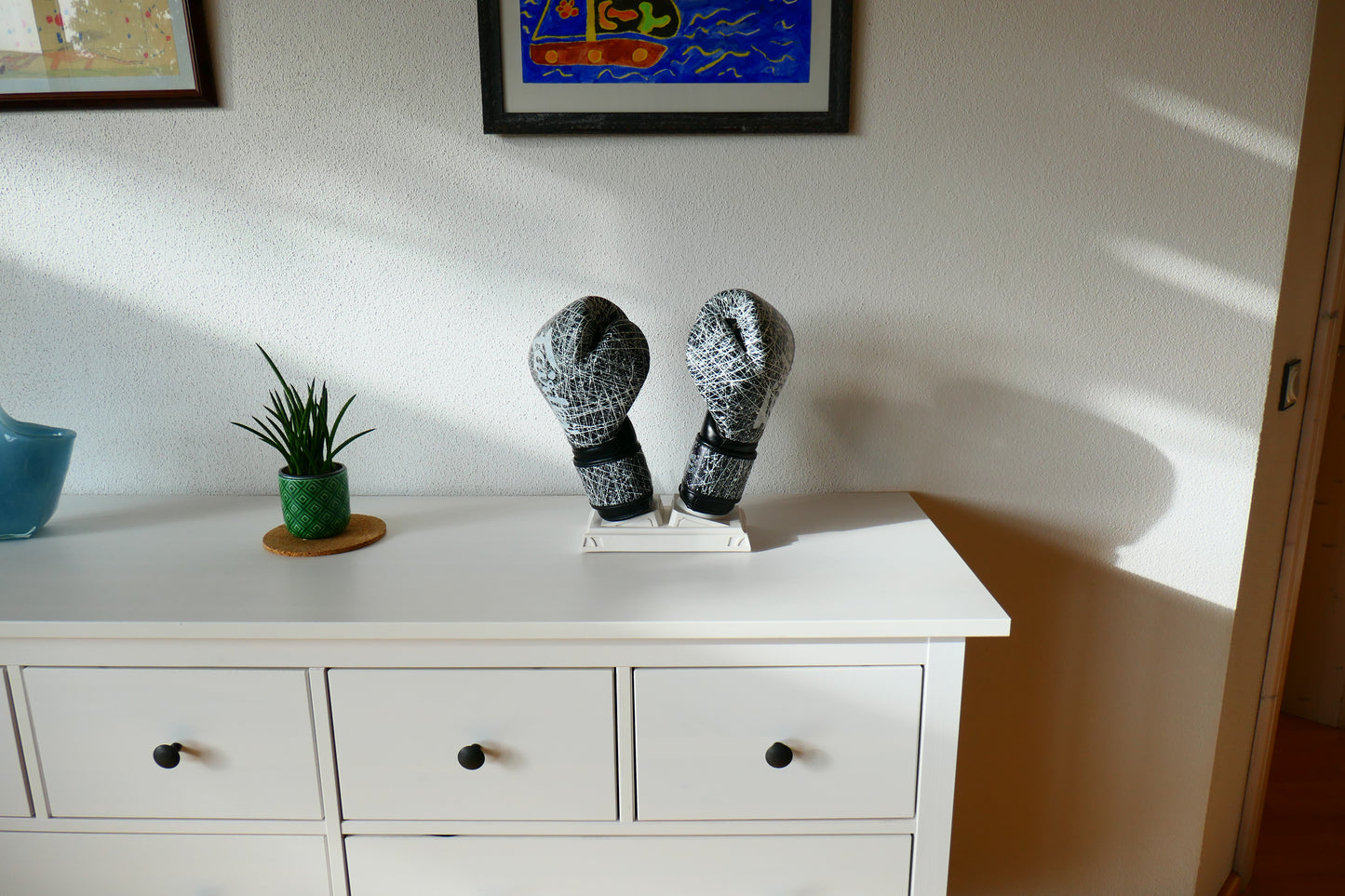 Weißer Nertas Boxhandschuhhalter/ Boxhandschuhständer ohne Personalisierung. Zu sehen mit Boxhandschuhen, auf einem Schrank mit Deko.