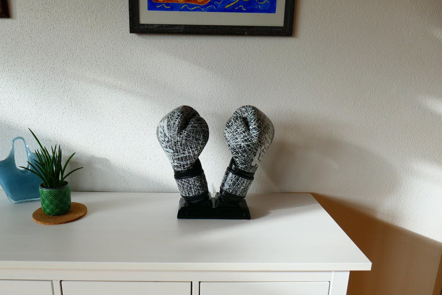 Schwarzer Nertas Boxhandschuhhalter/ Boxhandschuhständer ohne Personalisierung. Zu sehen mit Boxhandschuhen, auf einem Schrank mit Deko.